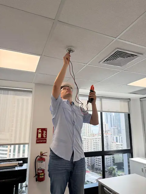 Técnico probando un detector de humo en el cielo raso de una oficina